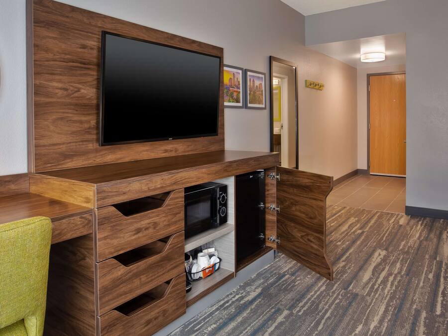 A hotel room with a wooden entertainment unit, a flat-screen TV, a microwave, and a small seating area with a green chair.