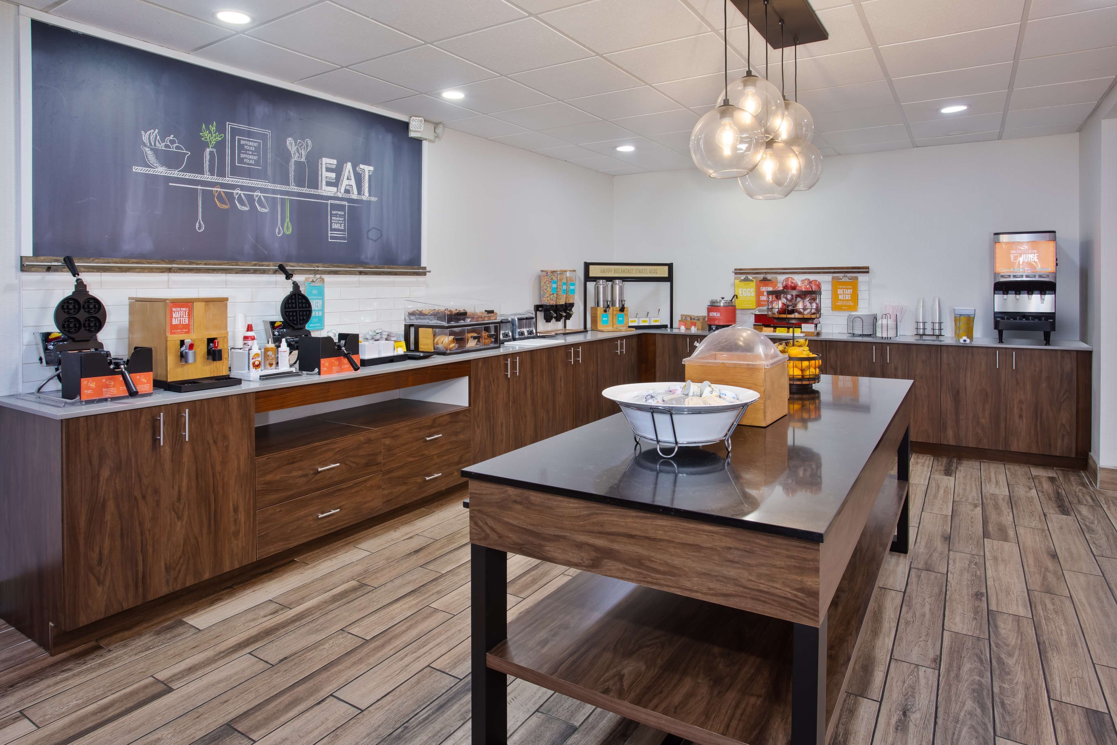 A modern kitchen area with a chalkboard menu, a coffee machine, and a variety of food items on display.
