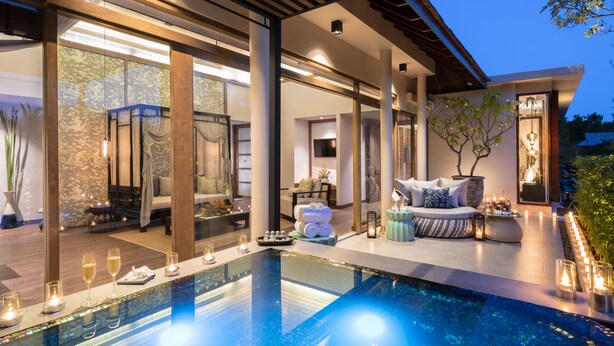 Un área de piscina moderna al aire libre con cerramiento de vidrio, asientos e iluminación ambiental.