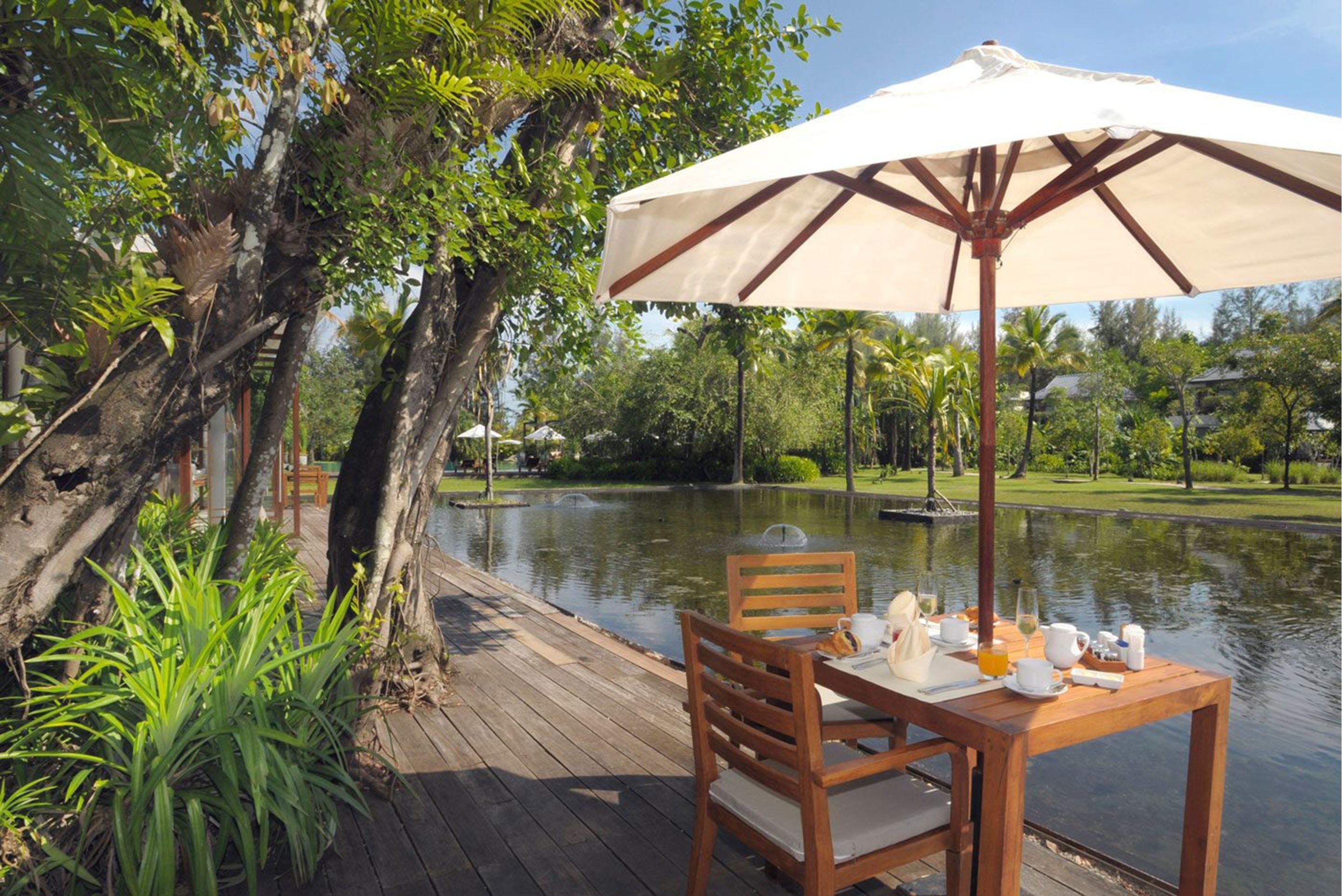 A wooden deck with a table and chairs, an umbrella, and a view of a lake with trees and a distant building.