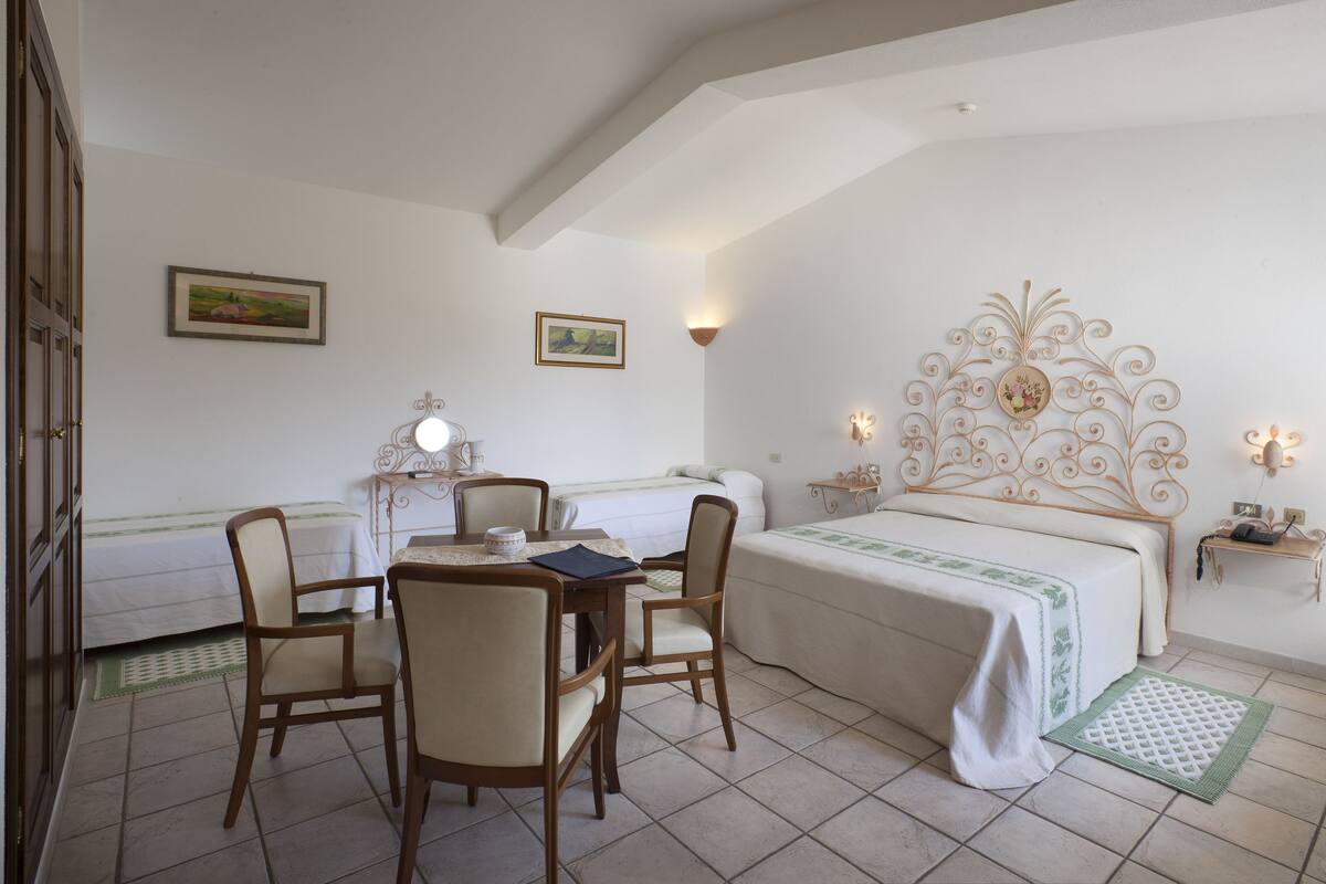 A bedroom with a bed, two chairs, a table, and a nightstand.