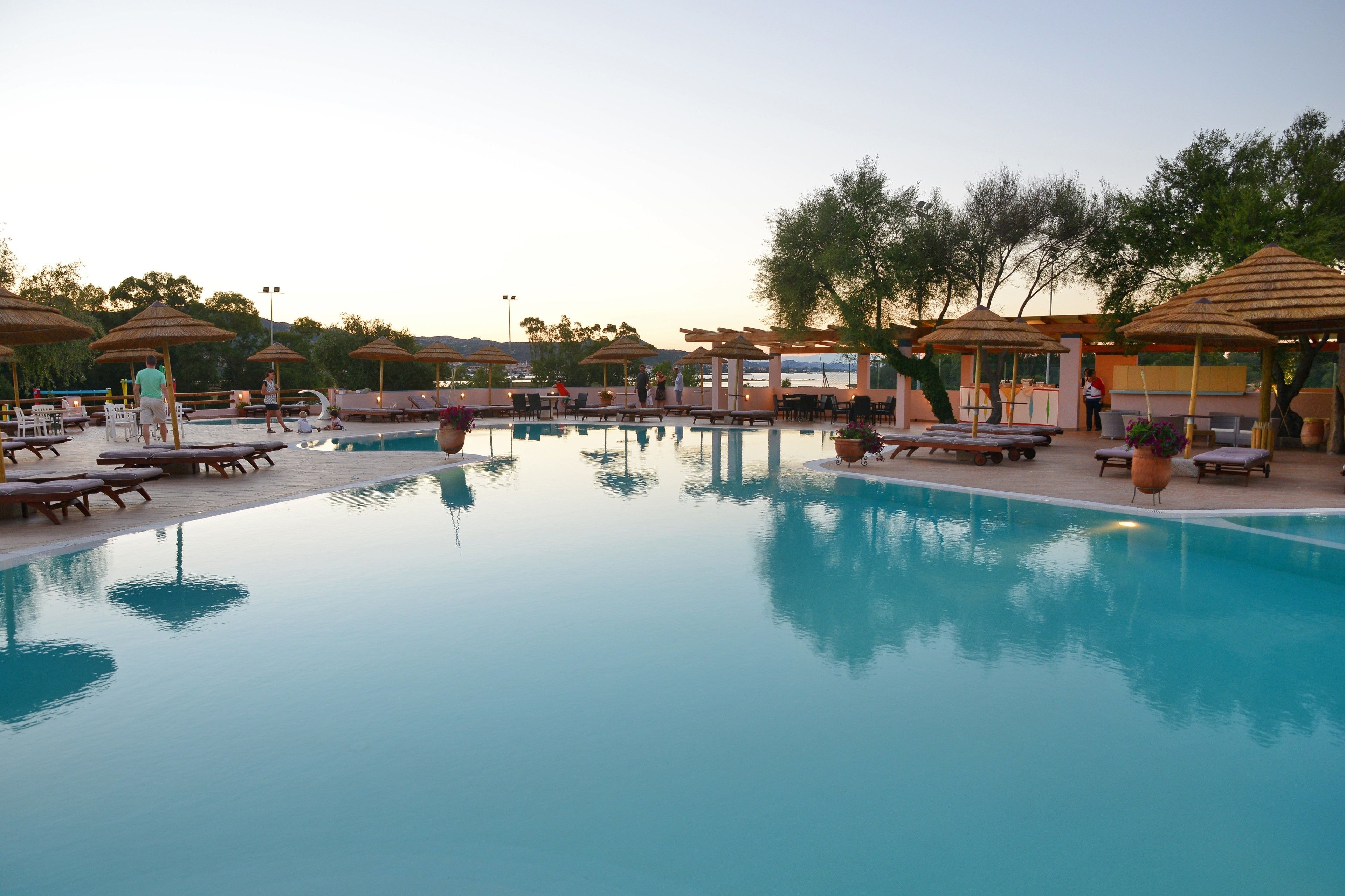 A pool area with lounge chairs and umbrellas, surrounded by trees.
