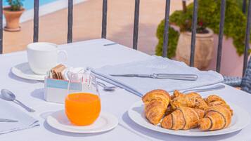 Disposição para o café da manhã com croissants e suco de laranja em uma mesa à beira da piscina.