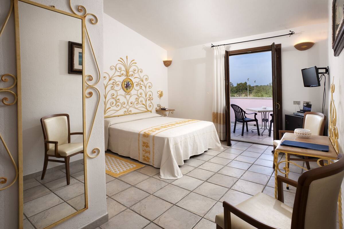 A hotel room with a bed, a desk, a chair, and a balcony with a table and chairs.