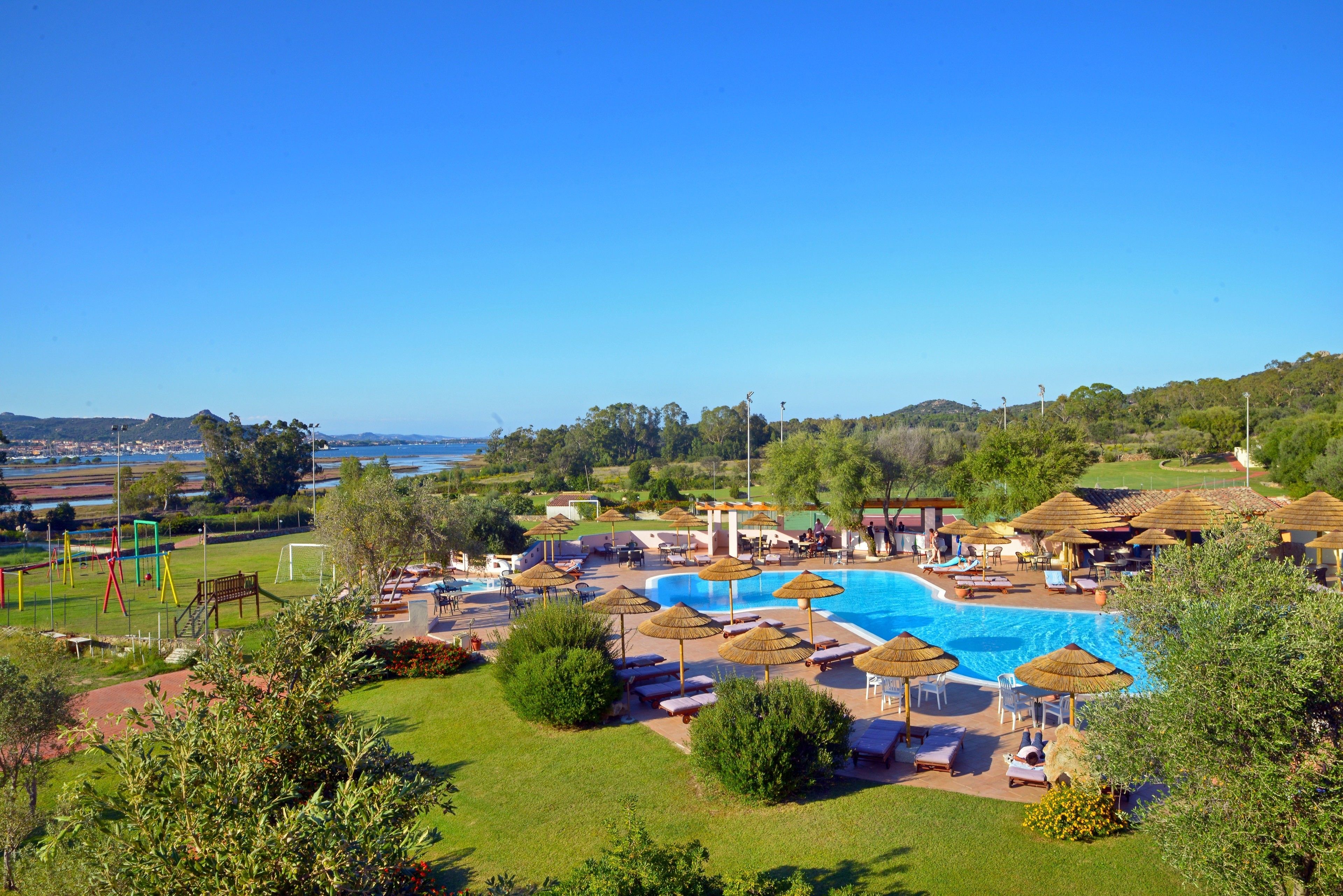 A resort with a swimming pool, sun loungers, umbrellas, and a view of the sea.