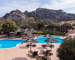 A pool area with lounge chairs and umbrellas, surrounded by trees and a mountain backdrop. - Felix Hotels - Hotel Airone (Arzachena)