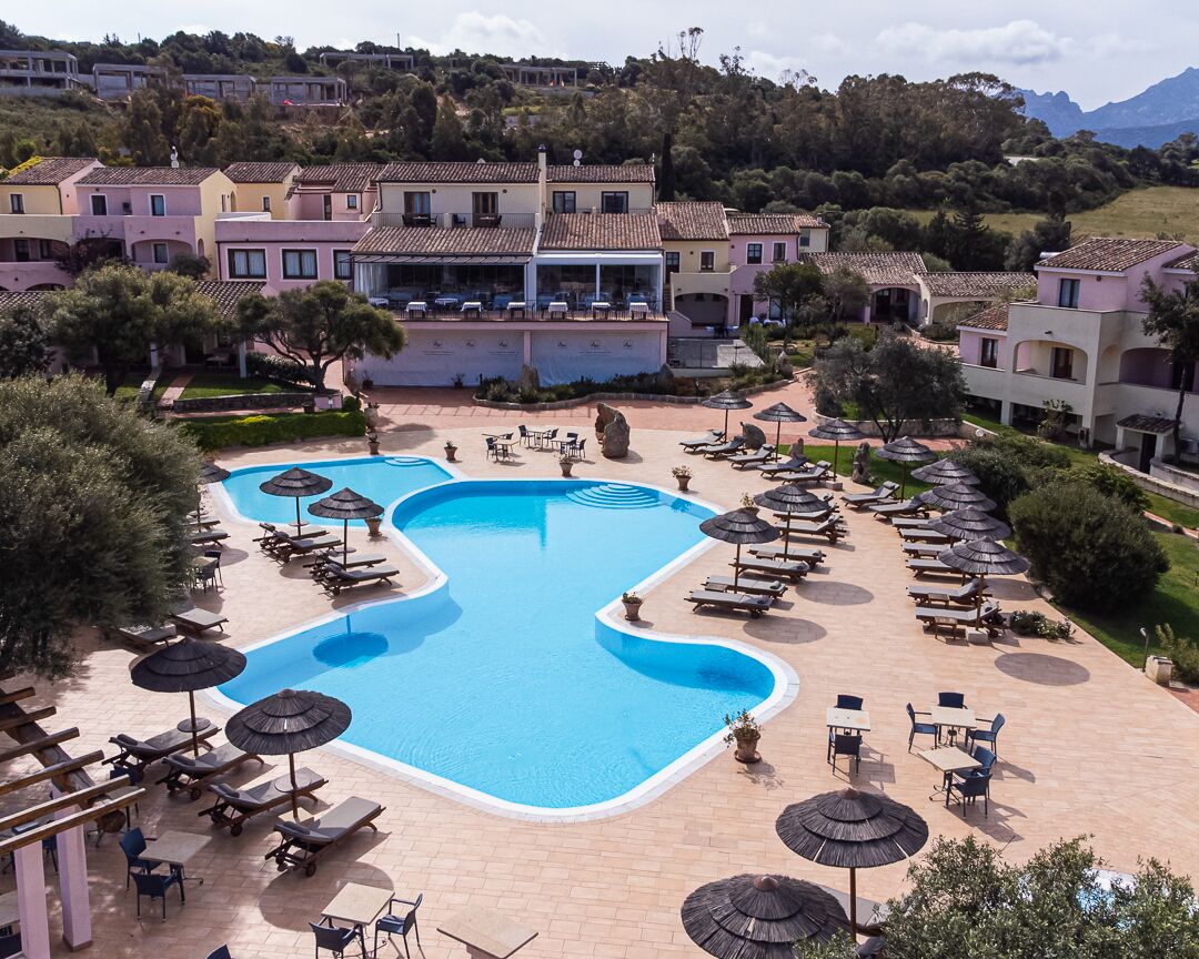 A resort with a large swimming pool, sun loungers, and umbrellas.