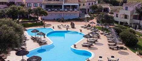 A resort with a large swimming pool, sun loungers, and umbrellas.