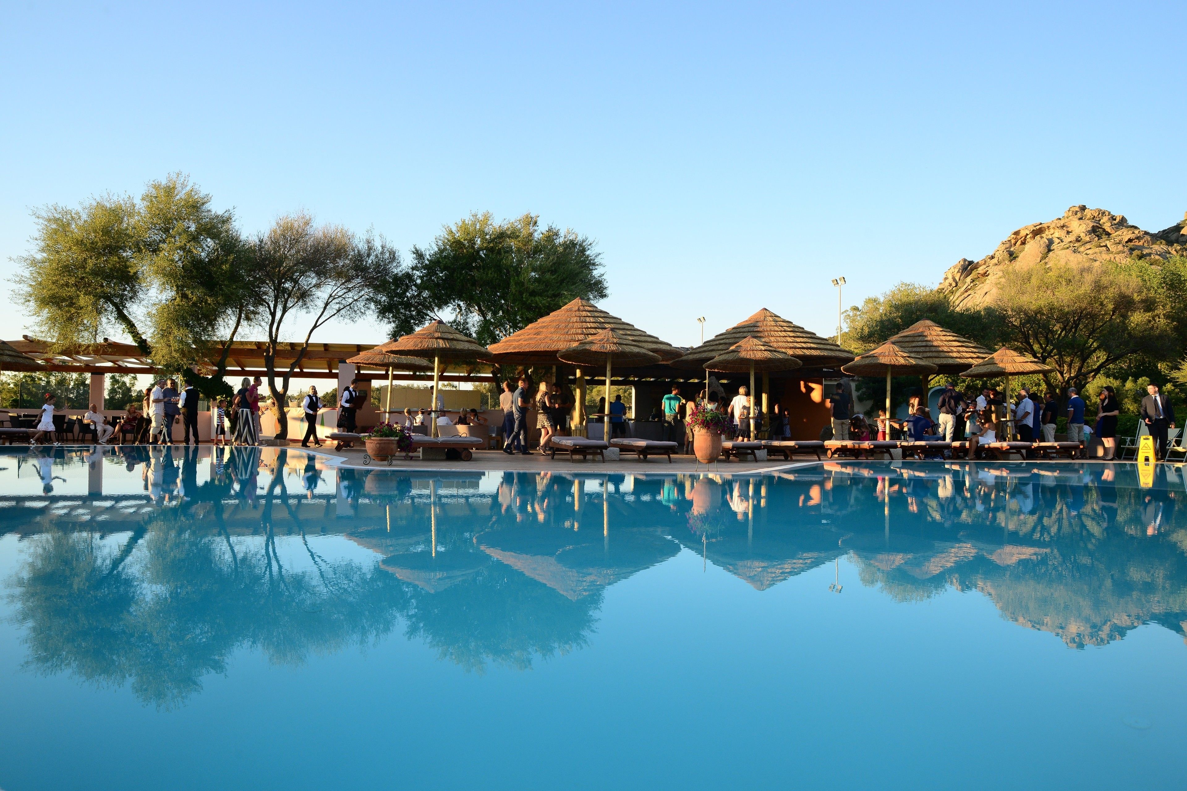 A pool area with umbrellas and lounge chairs, surrounded by trees and a mountainous backdrop.