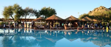 A pool area with umbrellas and lounge chairs, surrounded by trees and a mountainous backdrop.