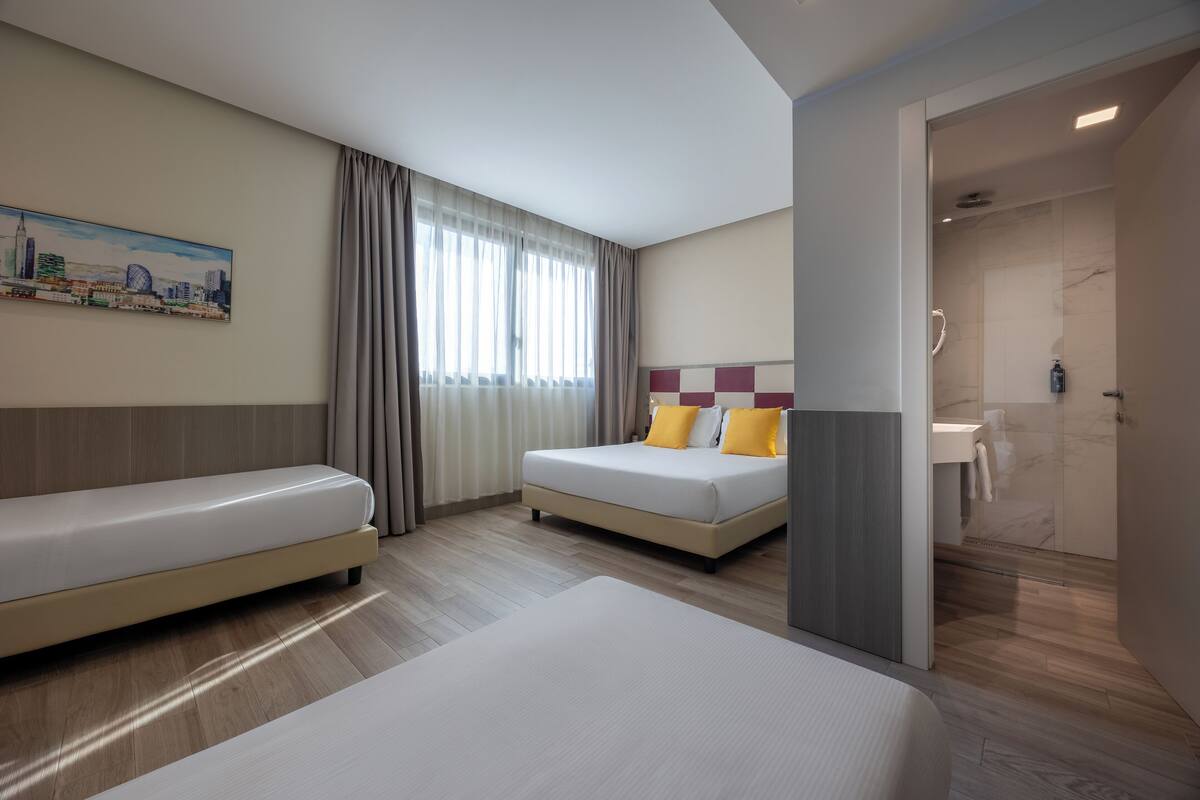 Ein Hotelzimmer mit zwei Betten, einem Bild an der Wand und einem durch eine offene Tür einsehbaren Badezimmer.