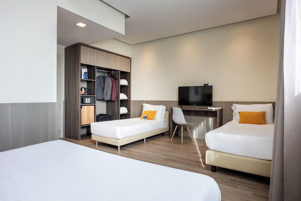 A hotel room with two beds, a TV, a desk, and a wardrobe.