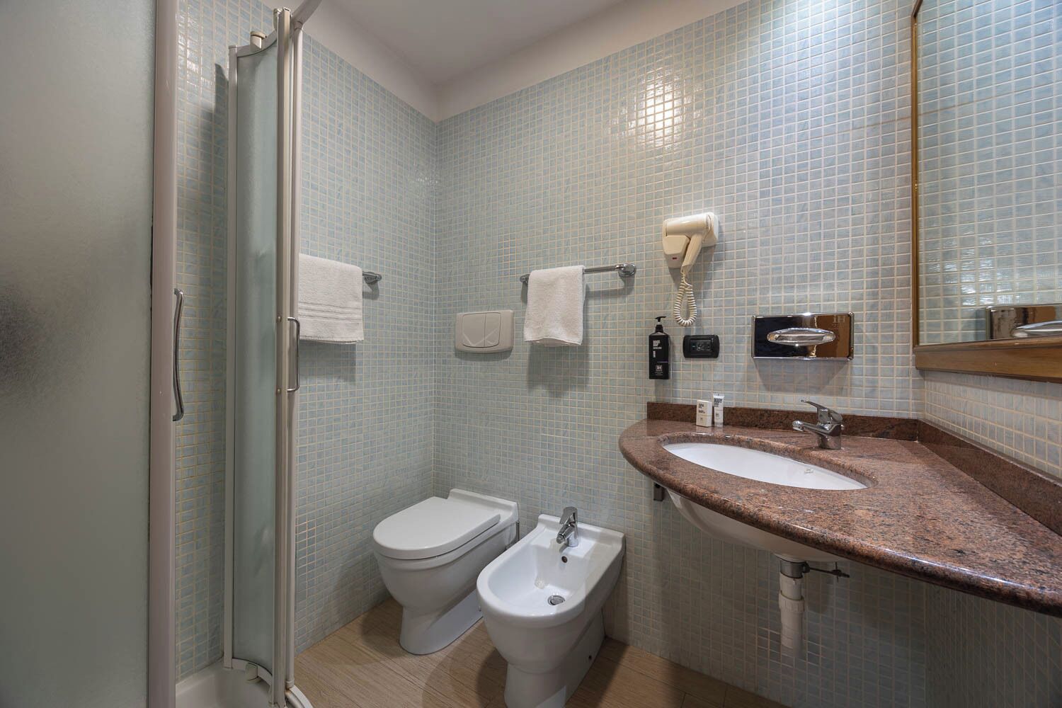 Une salle de bain avec une douche, deux toilettes, un lavabo et un miroir.
