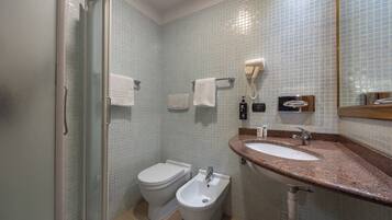 Un baño con ducha, dos inodoros, un lavamanos y un espejo.