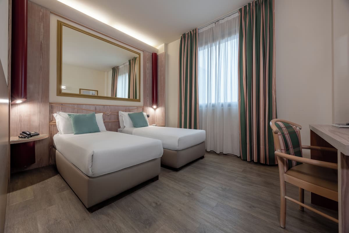 Ein Hotelzimmer mit zwei Betten, einem Schreibtisch, einem Stuhl, einem Telefon und einem großen Spiegel.