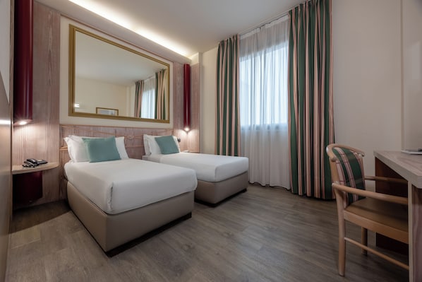 A hotel room with two beds, a desk, a chair, a phone, and a large mirror.