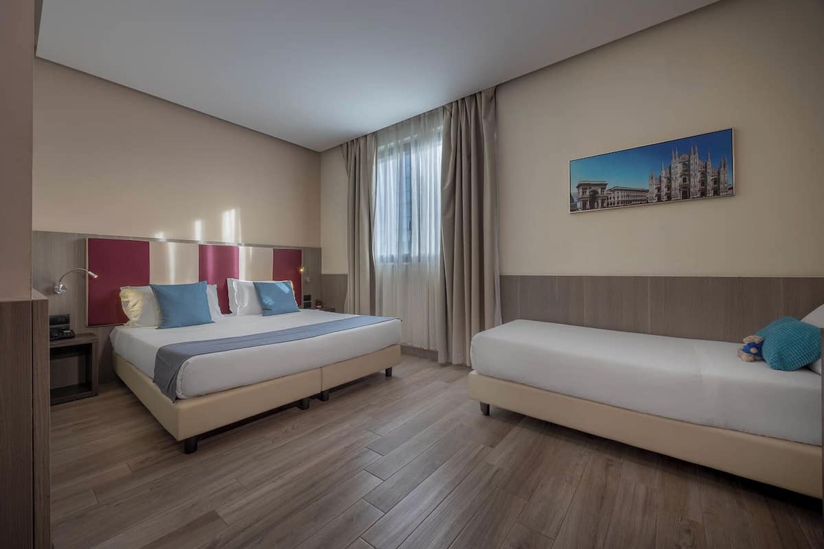 Ein Hotelzimmer mit einem großen Bett, einer kleinen Sitzecke, einem Nachttisch, einer Lampe und einem Gemälde an der Wand.