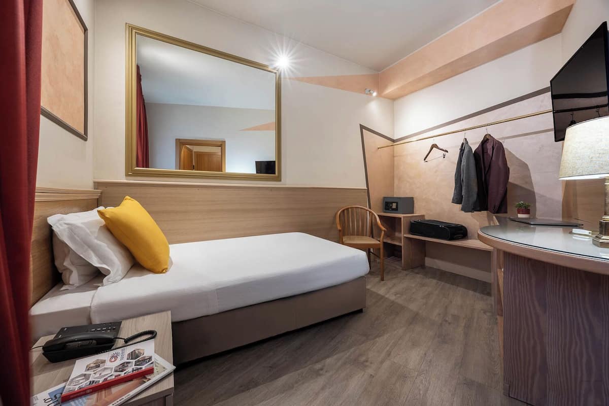 Ein Hotelzimmer mit Bett, Schreibtisch, Stuhl, Spiegel und Lampe.