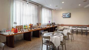 Ein reichhaltiges Buffet mit verschiedenen Speisen und Beilagen, präsentiert auf einem langen Tisch in einem Raum mit Fliesenboden und weißen Wänden.