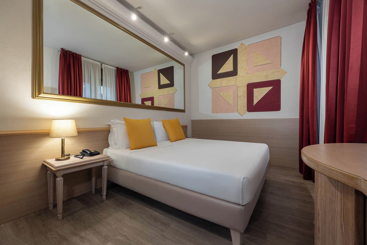A hotel room with a bed, bedside table, lamp, and a mirror.