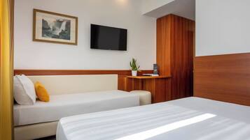 Habitación de hotel con cama, sofá, televisor montado en la pared y armario de madera.