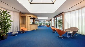 Eine moderne Hotelhalle mit einer zentralen Rezeption, einer Sitzecke und großen Fenstern für natürliches Licht.