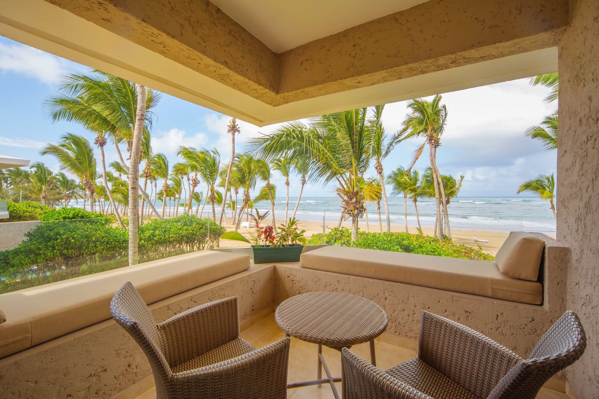 Een balkon met rieten meubilair, uitzicht op het strand en palmbomen.