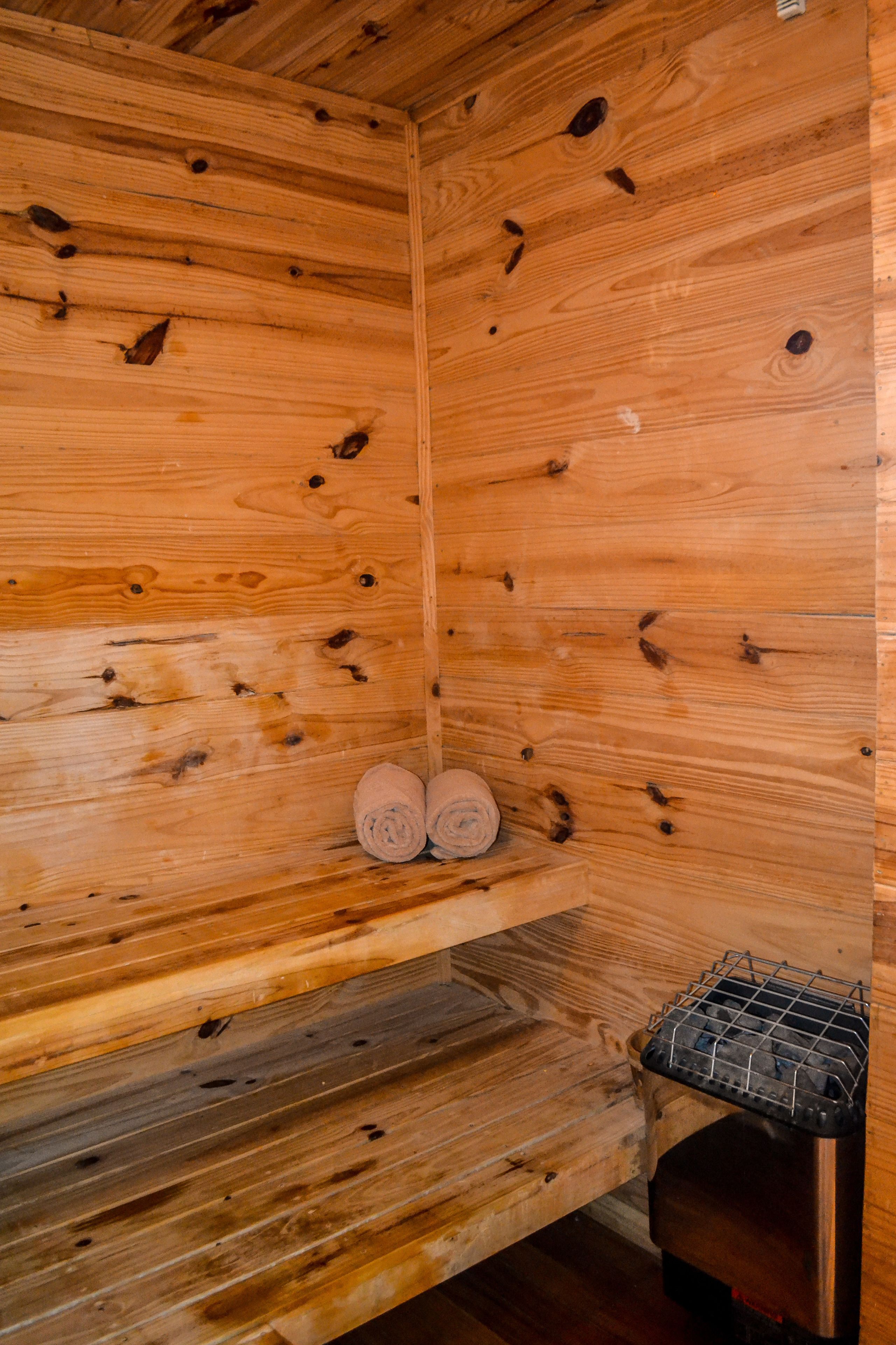 A wooden cabin interior with a bench, a small shelf with rolled towels, and a heater.