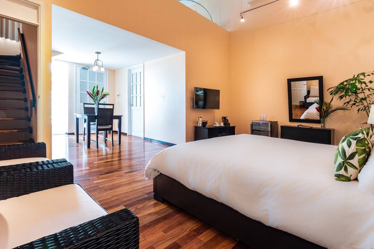 Un dormitorio moderno con una cama grande, un televisor, un escritorio con silla y una escalera.