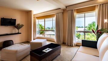 A modern hotel room with a large window, a flat-screen TV, a sofa, a coffee table, and a small side table.
