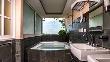 Un baño moderno con una bañera grande, dos lavamanos, una planta en maceta y vistas a zonas verdes.