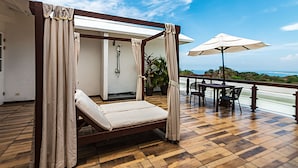 A bedroom with a wooden bed, a shower, and a balcony with a table and chairs. - Gaia Hotel And Reserve - Adults Only (Quepos)