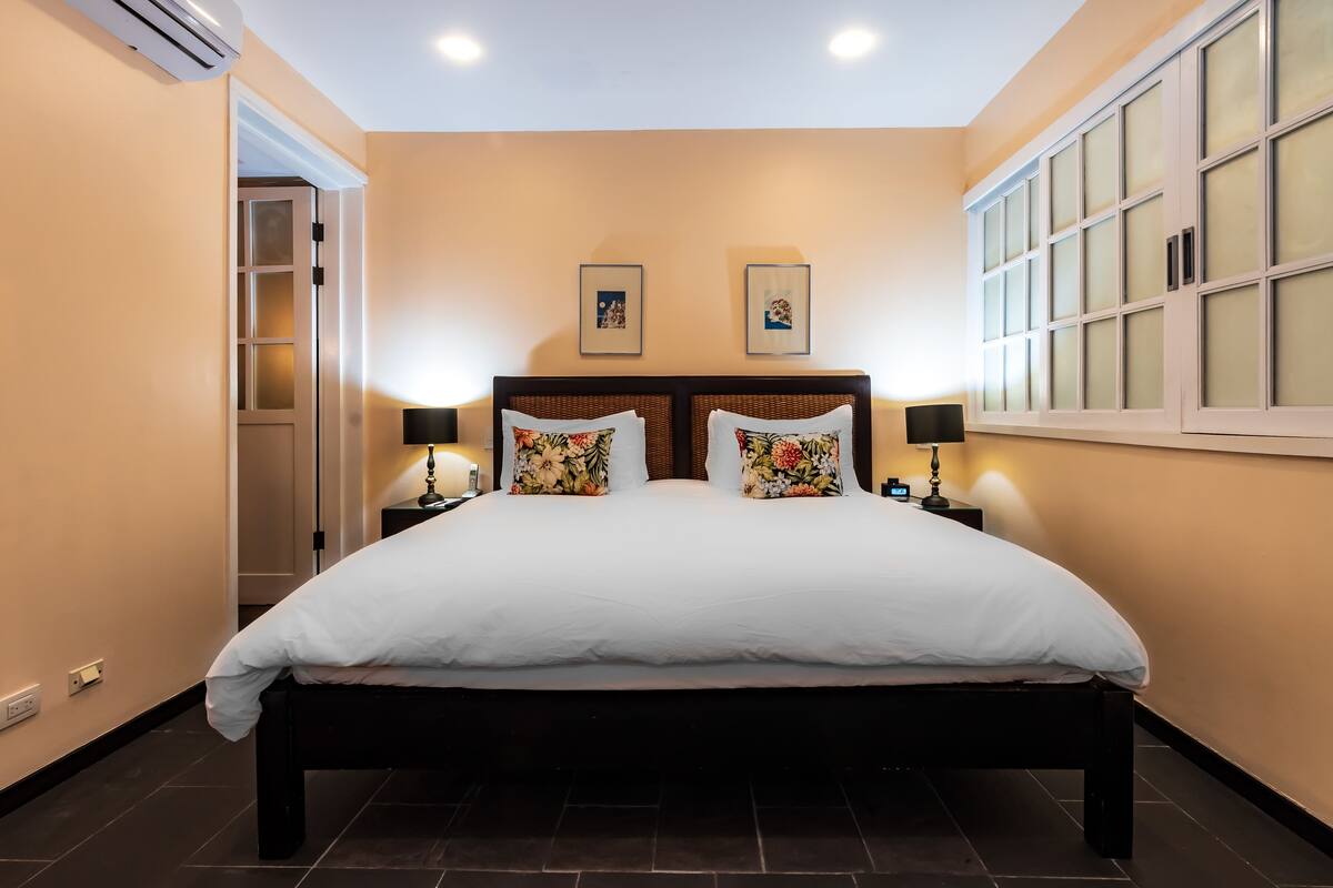 Un dormitorio con una cama grande, dos mesitas de noche con lámparas, un armario con puertas de vidrio esmerilado y dos cuadros enmarcados en la pared.