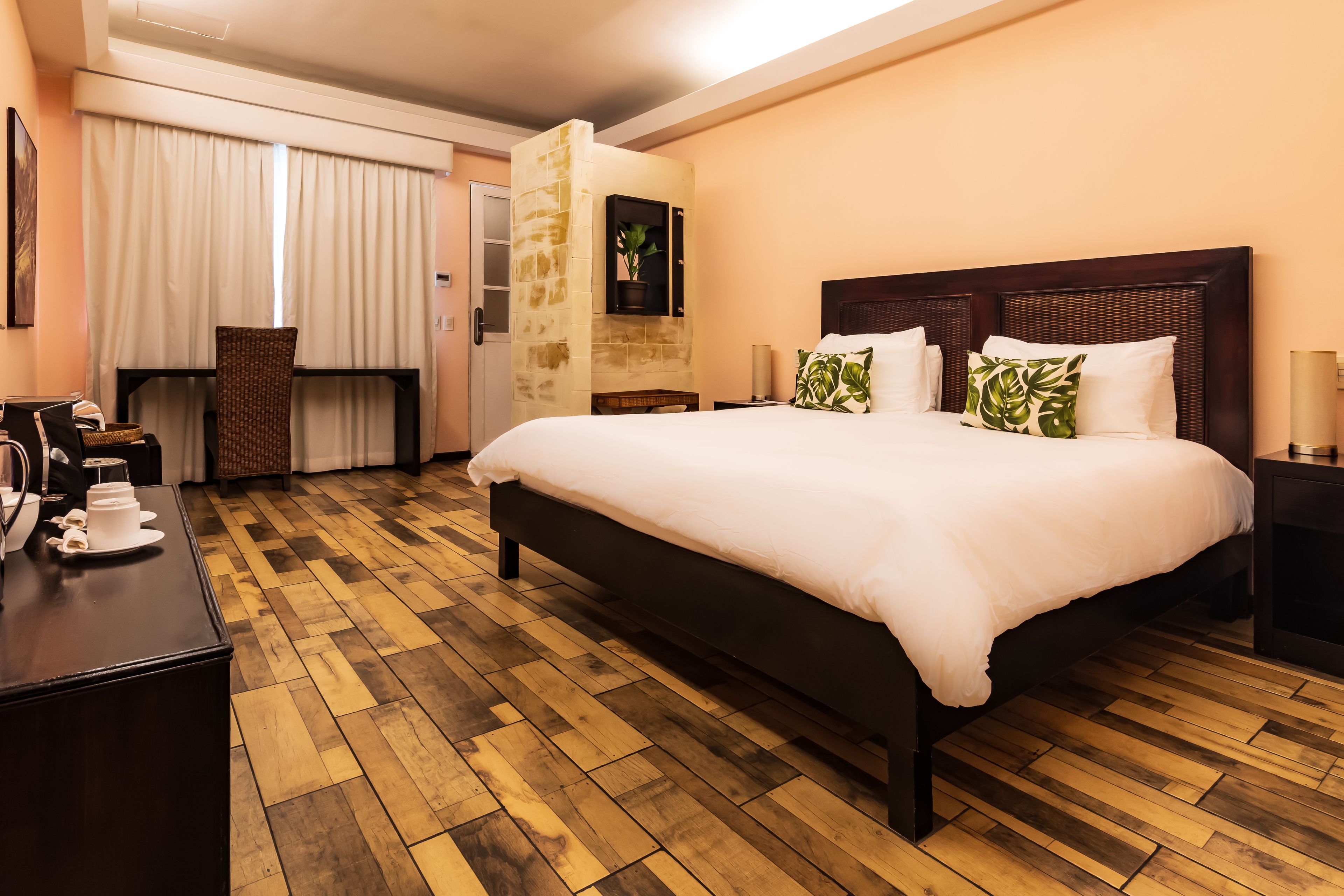 A hotel room with a large bed, a wooden floor, a desk with a chair, and a wall-mounted TV.
