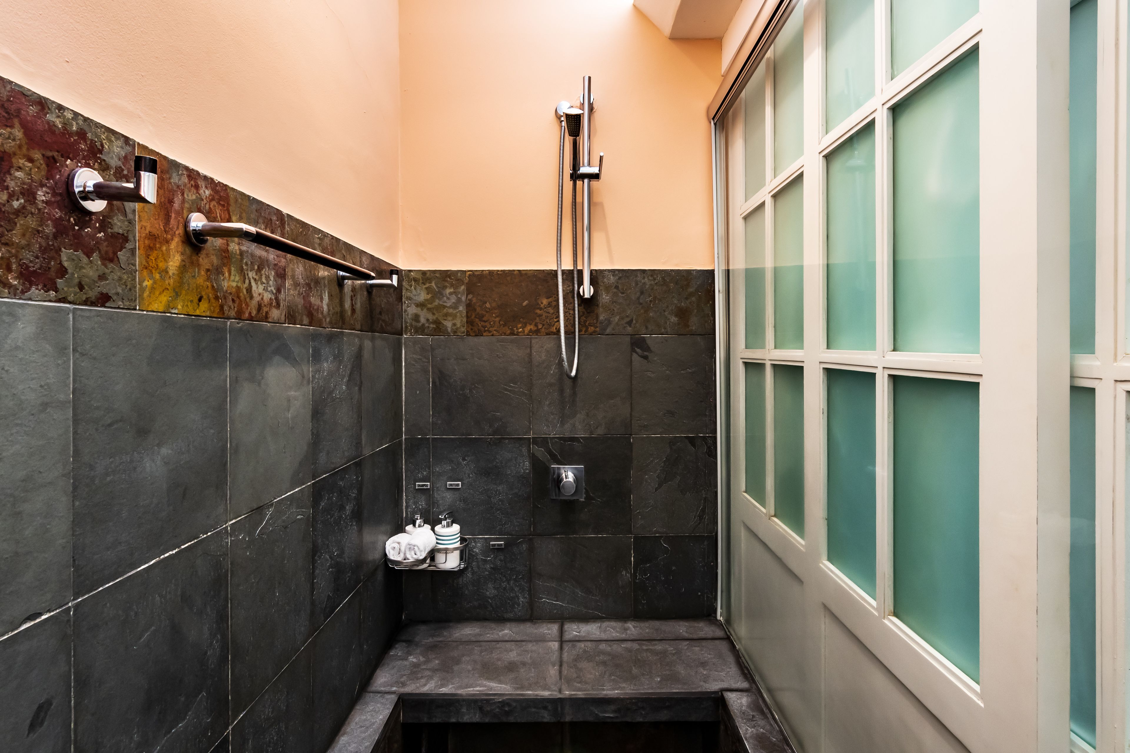 A small, enclosed shower area with a glass door, a towel rack, and a shelf with toiletries.