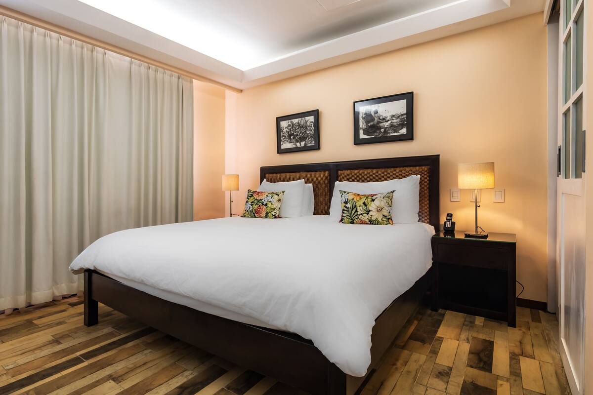 Una habitación de hotel con una cama grande, dos mesitas de noche y un ventanal con cortinas.