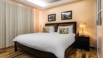 A hotel room with a large bed, two pillows, a nightstand with a lamp, and two framed pictures on the wall.