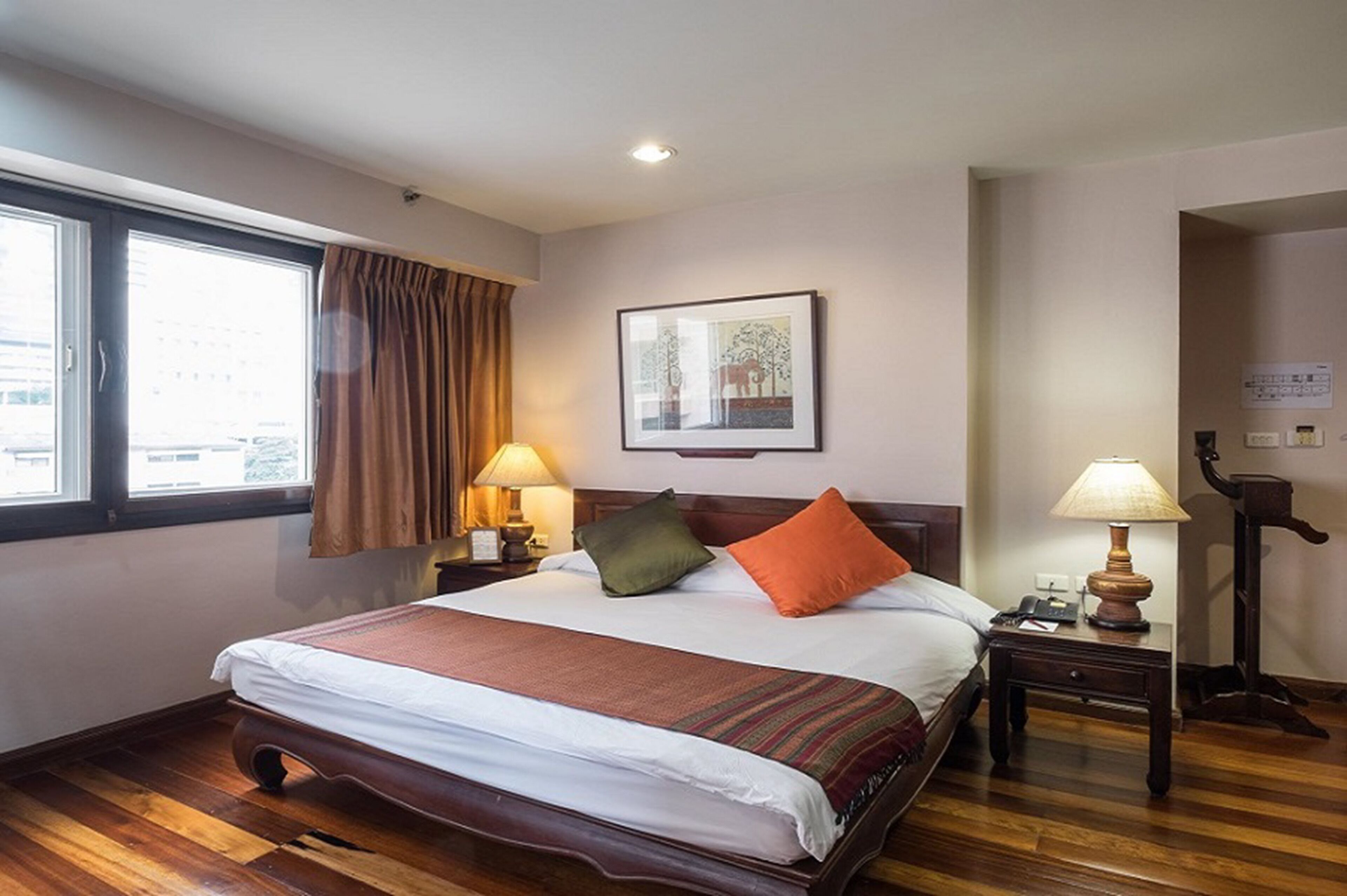 A hotel room with a large bed, two bedside lamps, a framed picture on the wall, and a window with curtains.