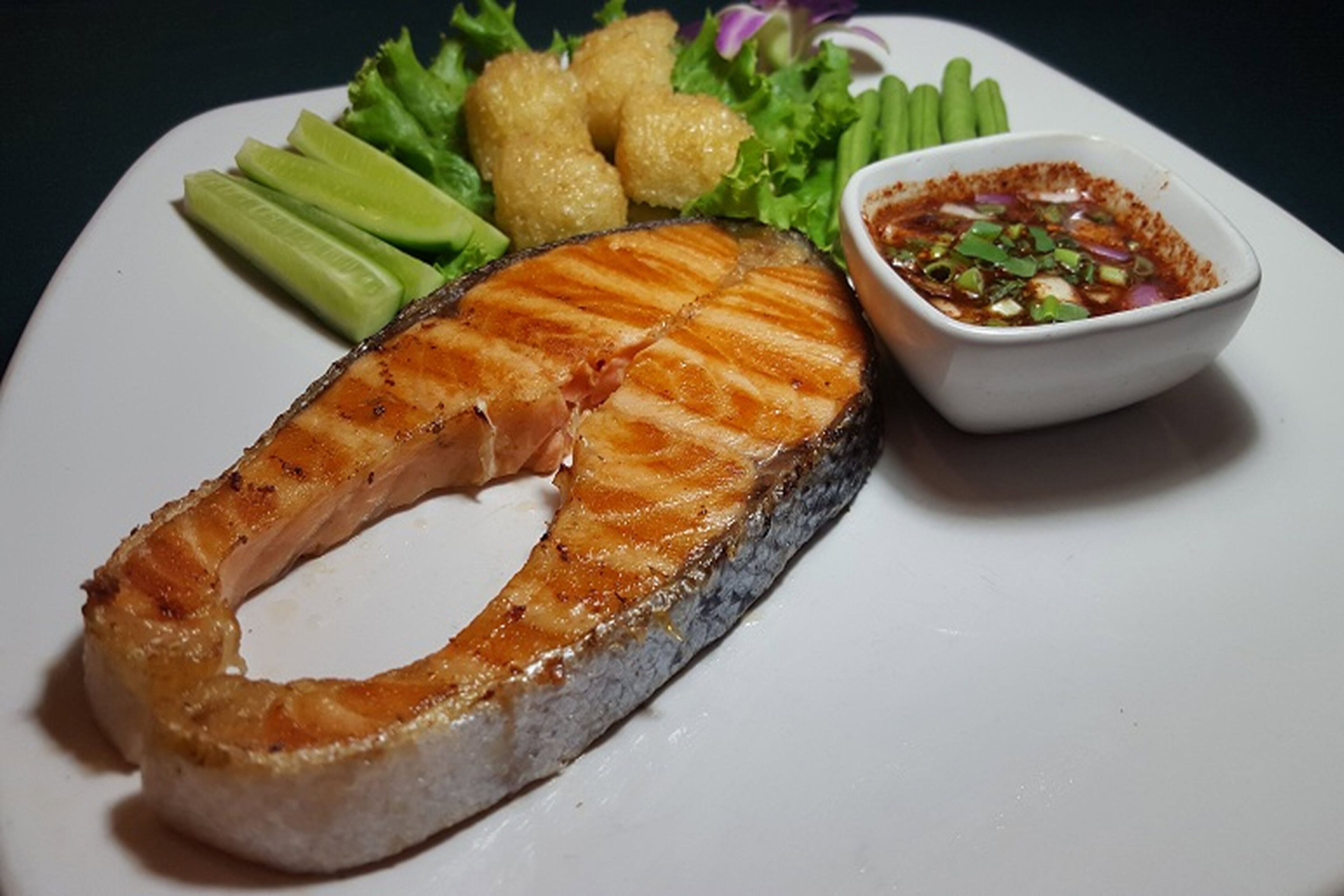 A plate with grilled salmon, green vegetables, and a side of dipping sauce.