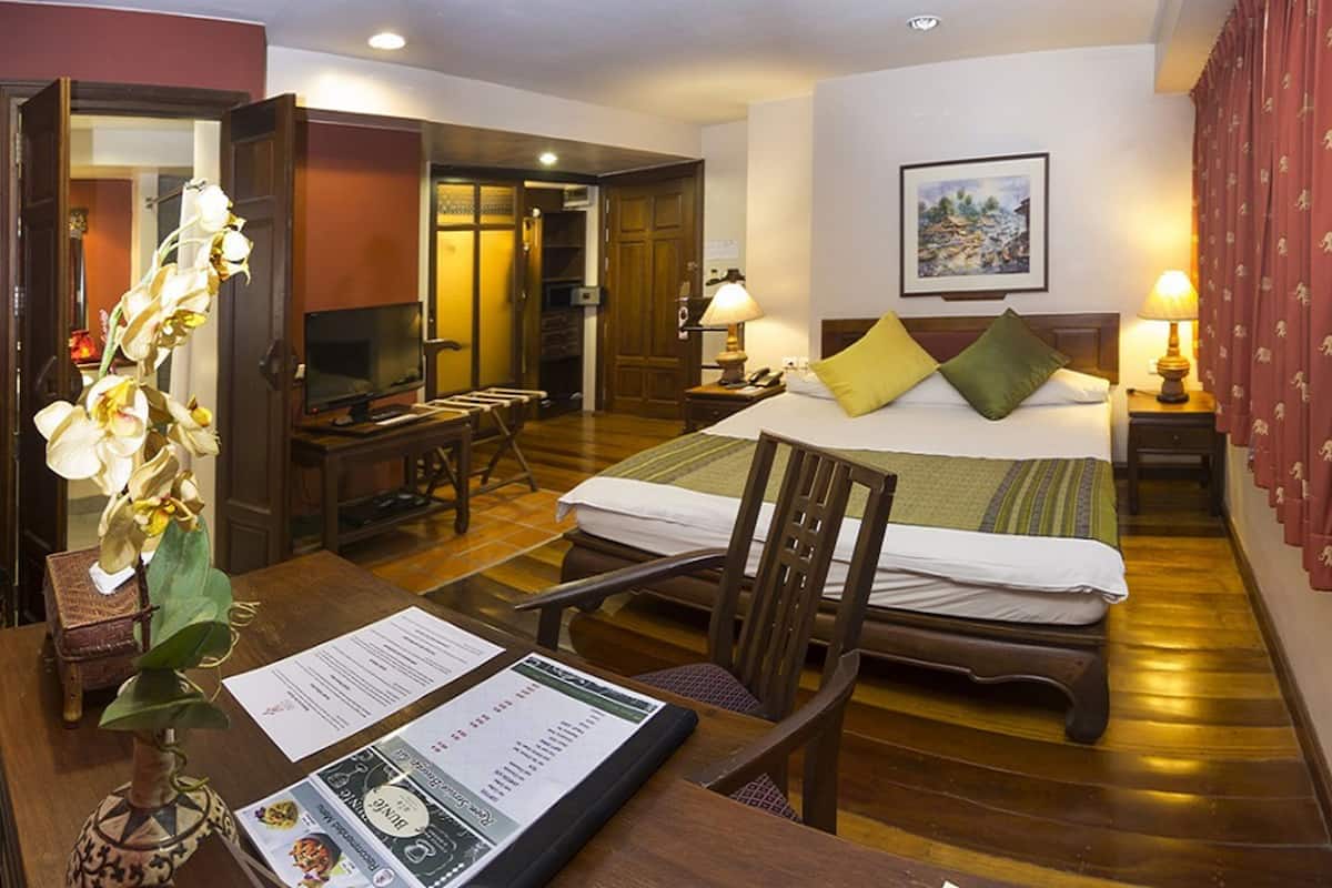 Ein Hotelzimmer mit einem Bett, Nachttischlampen, einem Schreibtisch mit Stuhl, einem Fernseher und einer Vase mit Blumen.