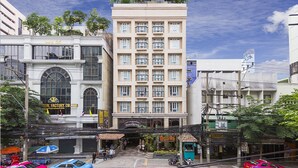 Un edificio de varios pisos con una entrada central, rodeado de tiendas y vehículos.
