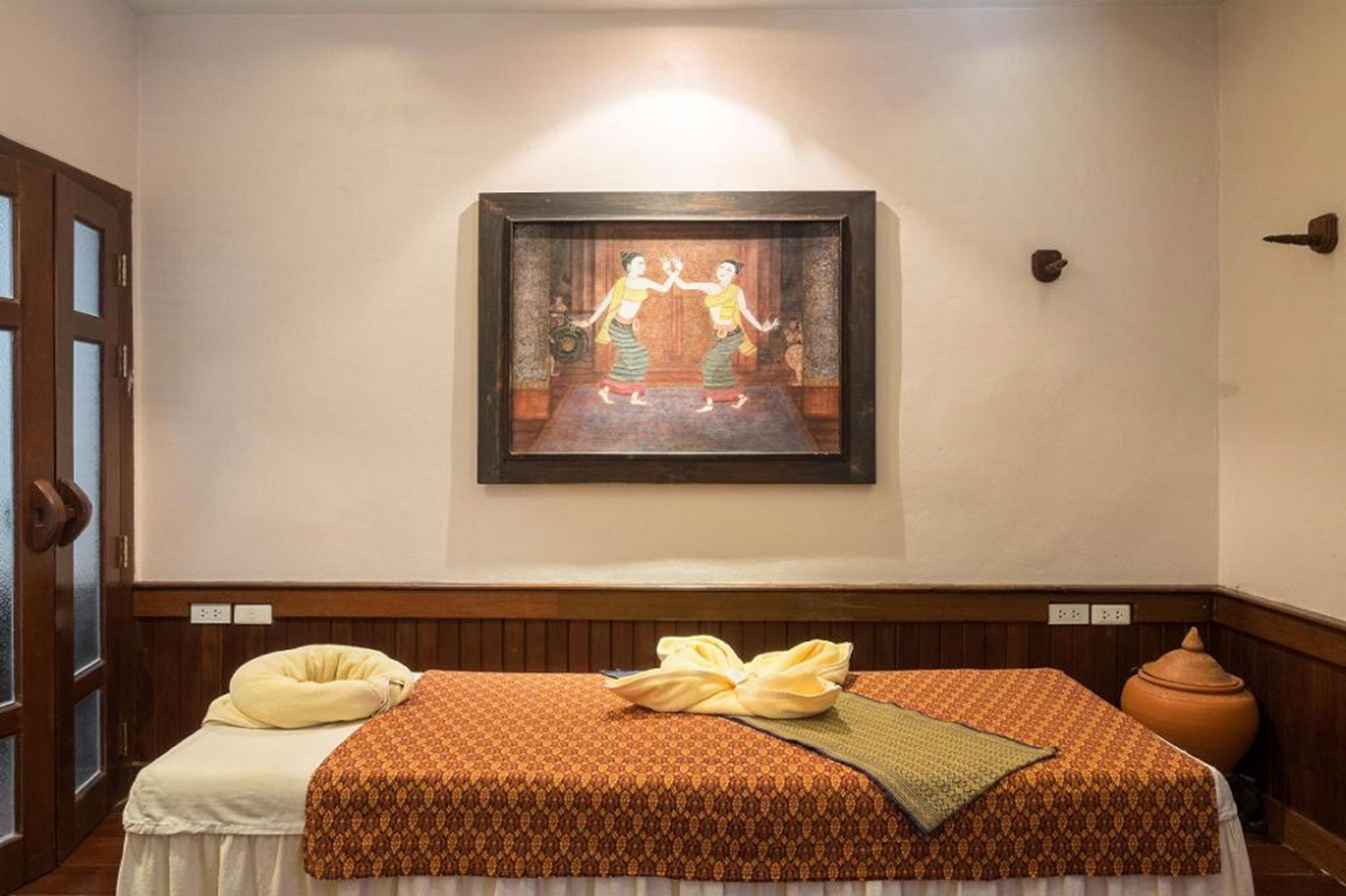 A room with a bed, a wall-mounted painting, a wooden bench, and a large pot.