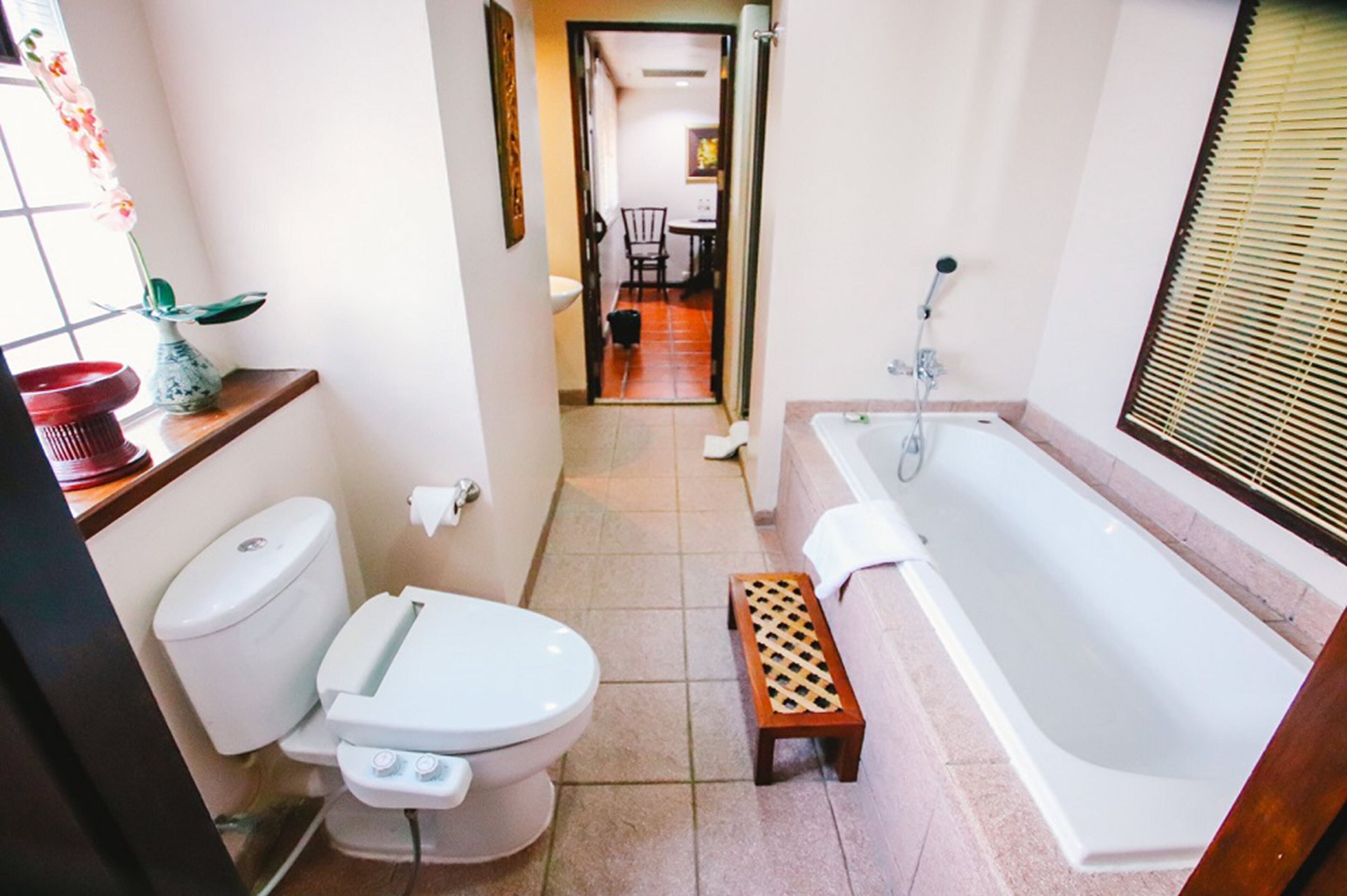 Ein Badezimmer mit Toilette, Bidet und Badewanne. Ein kleiner Holzschemel steht vor der Badewanne.