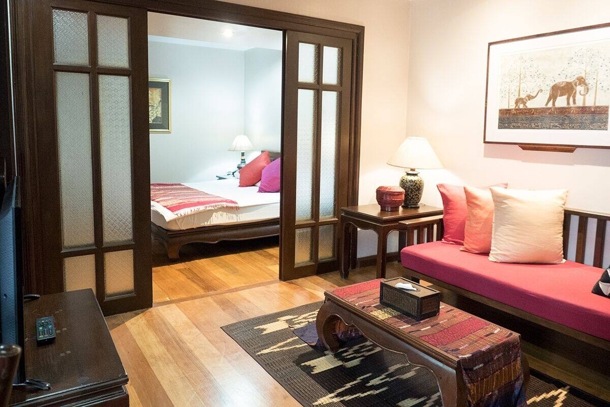 Ein Hotelzimmer mit Holzboden, einem Bett mit roter Bettwäsche, einem Sofa mit rosafarbenen Kissen, einem kleinen Tisch mit Lampe und einem gerahmten Bild an der Wand.