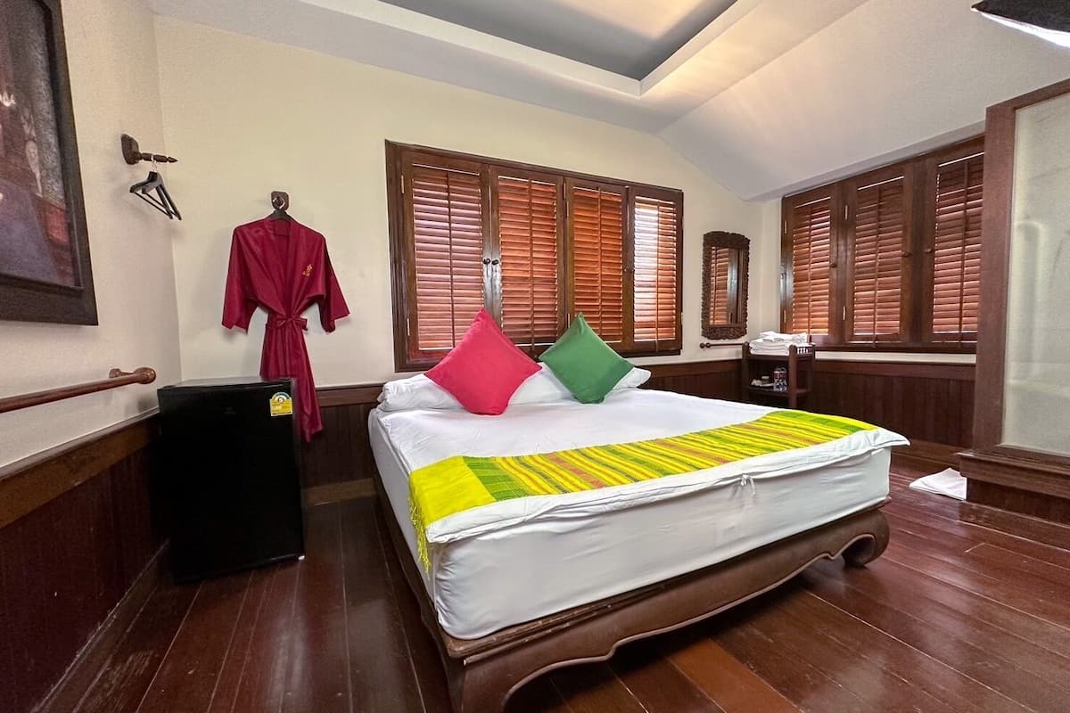 Ein Hotelzimmer mit einem hölzernen Bett, einem roten Bademantel und Holzjalousien.