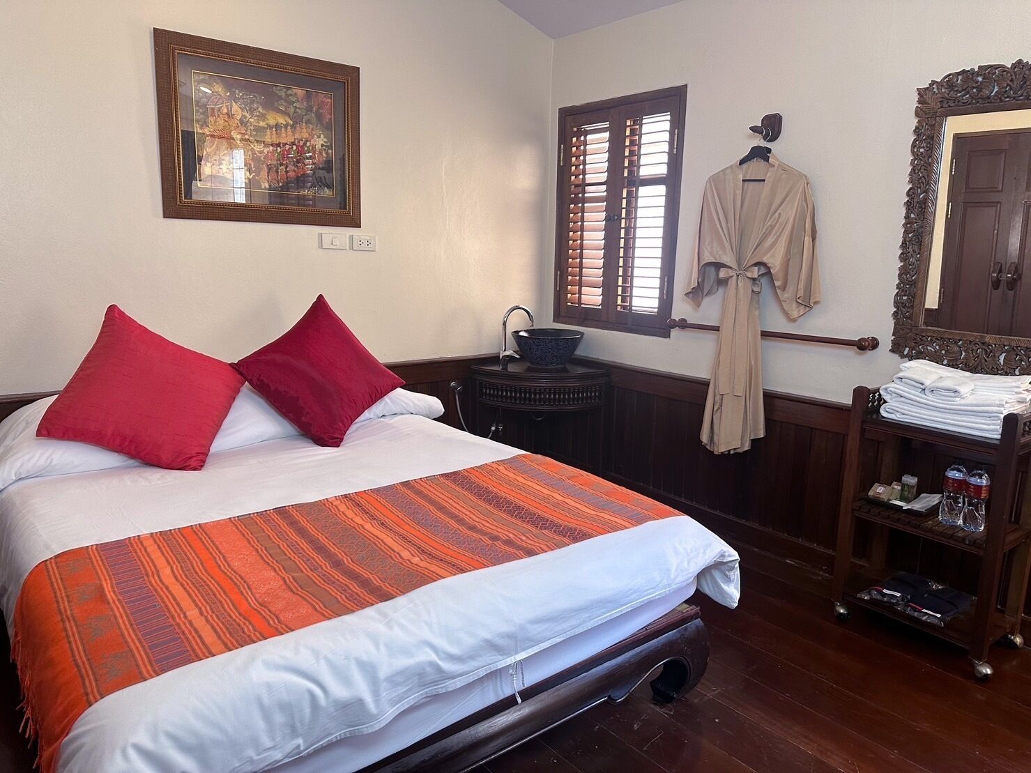A hotel room with a bed, a window with blinds, a sink, a robe, and a mirror.