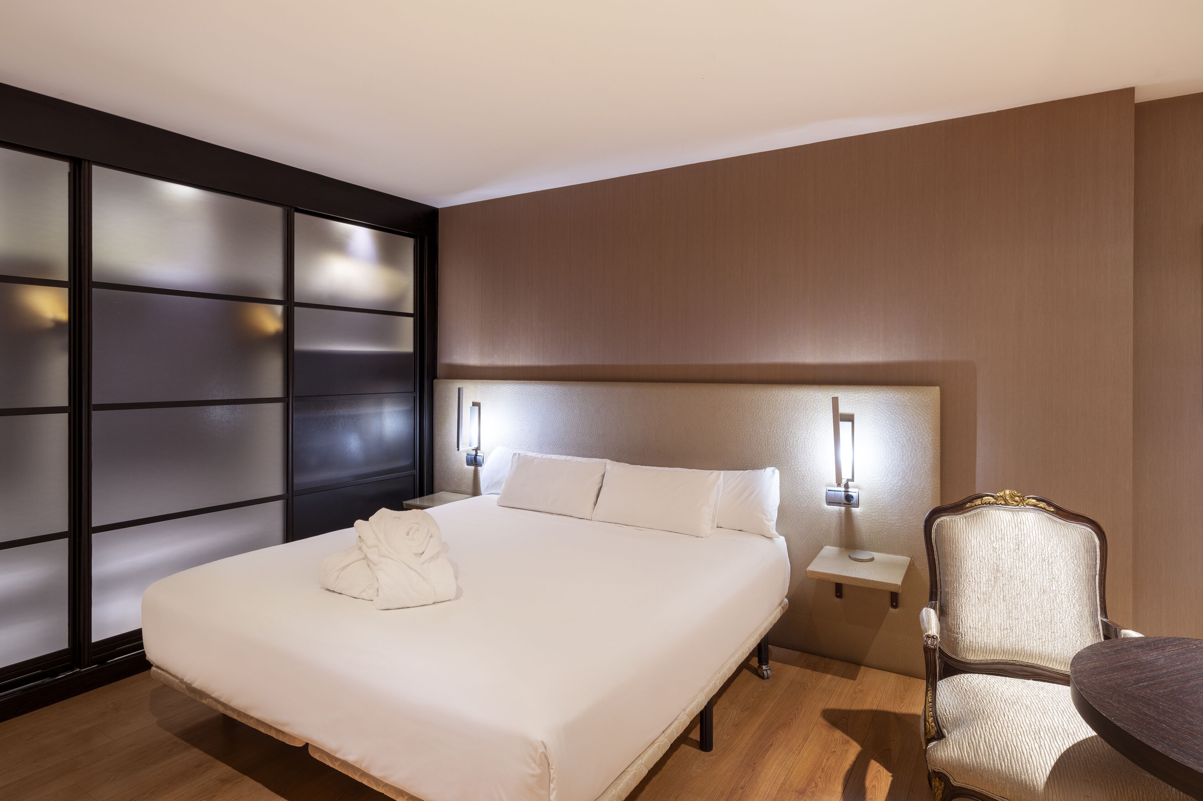 A hotel room with a large bed, a nightstand, a chair, and a wall with a unique design.