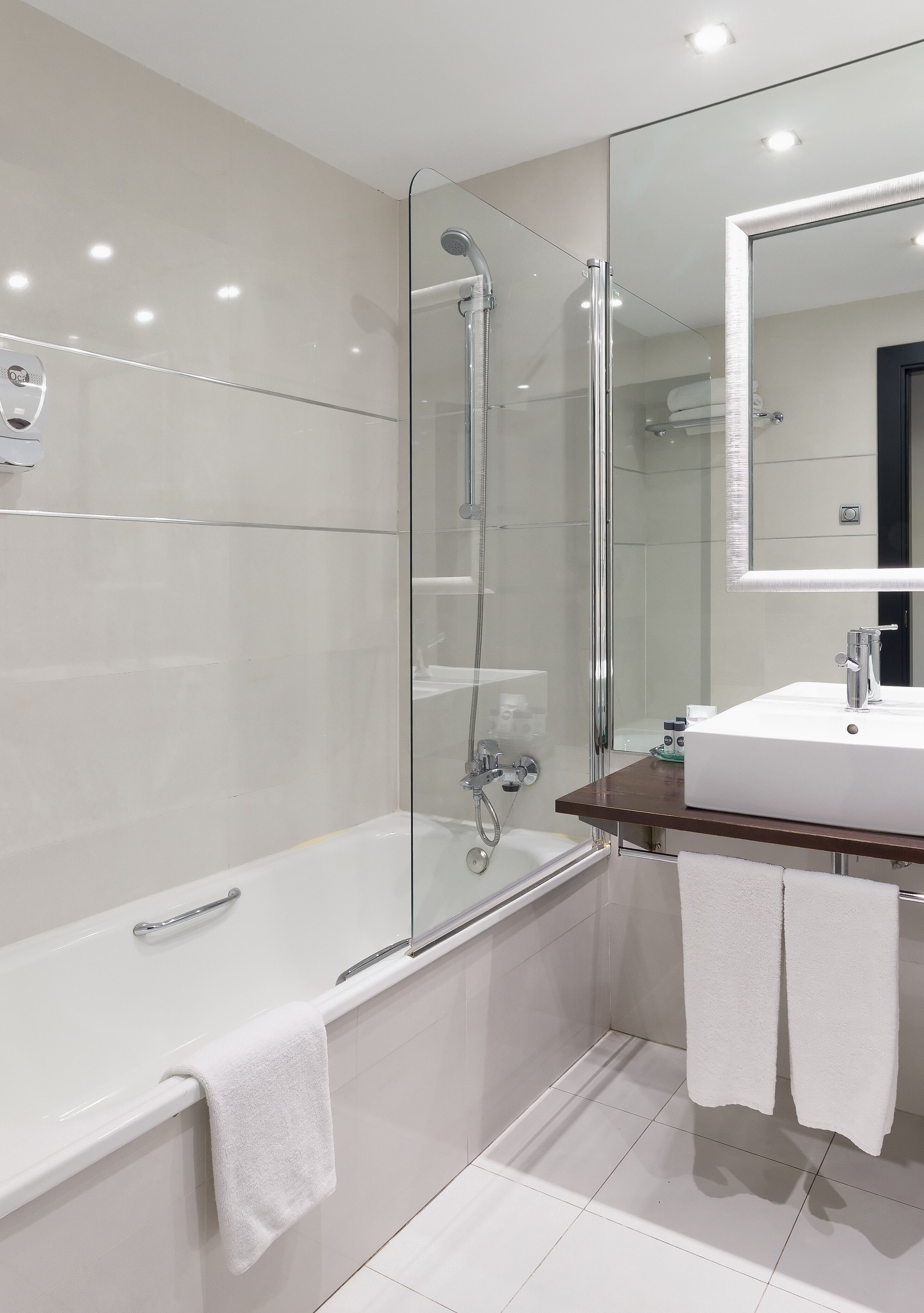 Un baño moderno con ducha envuelta en vidrio, bañera blanca y tocador de madera con espejo.