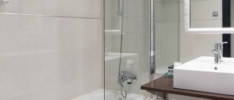 Un baño moderno con ducha envuelta en vidrio, bañera blanca y tocador de madera con espejo.