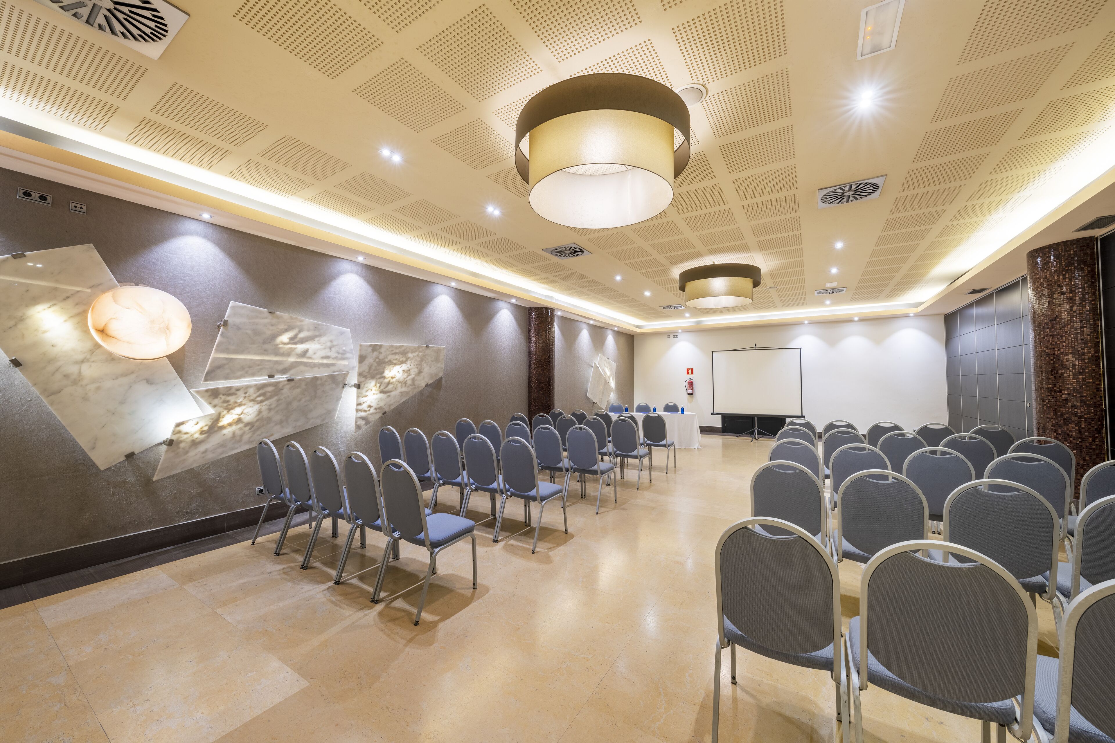 A conference room with rows of chairs, a projector screen, and a large abstract wall art piece.